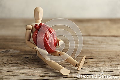 Wooden toy man holds a heart. Donor and transplant, symptoms of an attack. Surgical Assistance Stock Photo