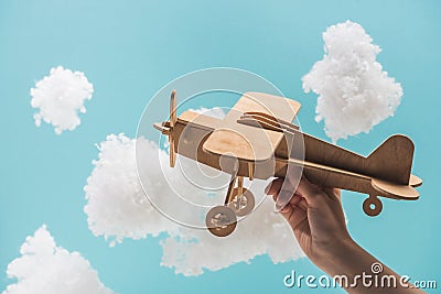 Wooden toy plane flying among white fluffy clouds made of cotton wool isolated on blue Stock Photo