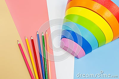 Wooden toy rainbow, arc and pencils on pink blue white orange background. Back to school background. Flat lay, top view. Education Stock Photo