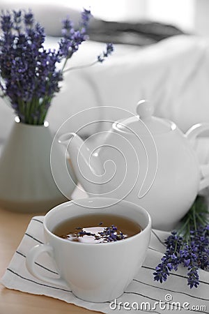 Wooden tray with cup of hot tea and lavender flowers on bed, closeup. Tasty breakfast Stock Photo