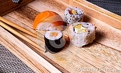 Wooden tray with four pieces of sushi rolls and chopsticks laid on top Stock Photo