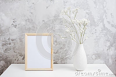 Wooden vertical white empty frame and bouquet of white small flowers gypsophila in vase on table on gray concrete wall Stock Photo