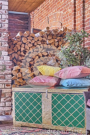 Woodpile of firewood, vintage chest and several colored pillows. Stock Photo