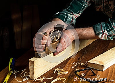 Woodworker using a hand plane to clean up a wooden board. Hands of the master closeup at work. Working environment in a carpentry Stock Photo