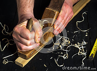 Woodworker using a hand plane to clean up a wooden board. Hands of the master closeup at work. Working environment in carpentry Stock Photo