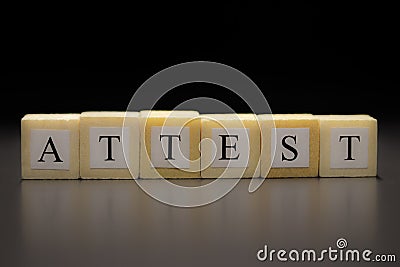The word ATTEST written on wooden cubes isolated on a black background Stock Photo