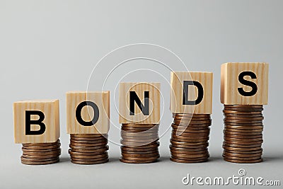 Word Bonds made of wooden cubes with letters on stacked coins against light grey background Stock Photo