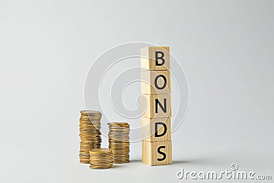 Word Bonds made of wooden cubes with letters and stacked coins on light grey background Stock Photo