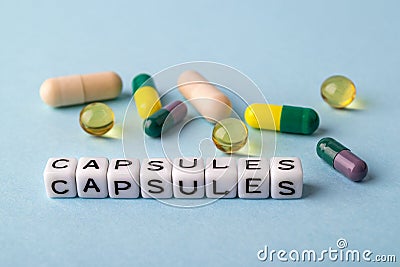 Word Capsules made of white cubes and different capsules on a blue medical background. To get sick, take pills or undergo Stock Photo