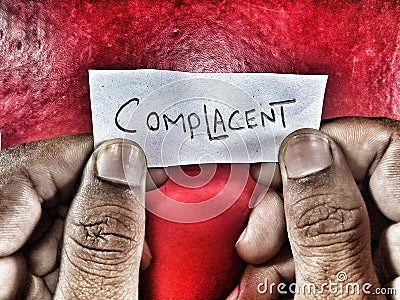 the word complacent written on the small paper red background and holding hands Stock Photo