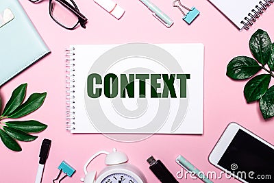 The word CONTEXT is written in a white notebook on a pink background surrounded by business accessories and green leaves Stock Photo