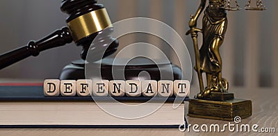 Word DEFENDANT composed of wooden dices. Wooden gavel and statue of Themis in the background Stock Photo