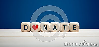 The word donate on wooden blocks with heart icon against blue background. Charity and donation Stock Photo