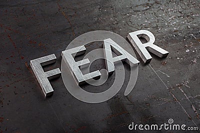 The word fear laid with silver letters on raw rusted steel sheet surface in diagonal slanted perspective Stock Photo