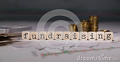 Word FUNDRAISING composed of wooden letter. Stacks of coins in the background Stock Photo