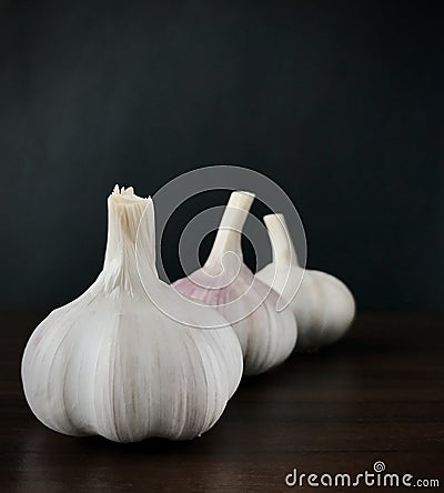 Three garlics on wood brown table, black background. Square. Stock Photo