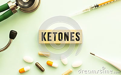 The word KETONES on a wooden cube with a stethoscope and pills. Medical concept. Flat lay. Stock Photo