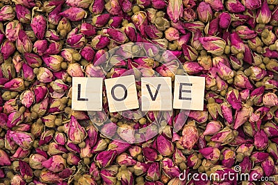 The word love on wooden tiles among many dried aromatic rose buds Stock Photo