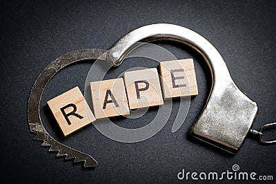 The word made of wooden letters - rape, on a black background in a handcuff. The concept of a crime Stock Photo