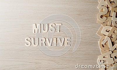 The word MUST SURVIVE, Wooden letters on a wooden table. Stock Photo