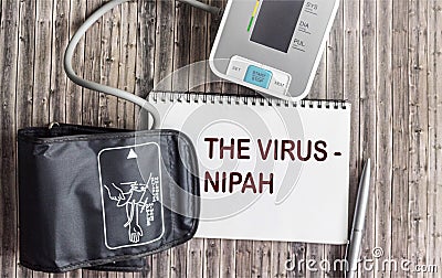 The word about the Nipah virus on a notepad, next to a blood pressure monitor on a wooden background Stock Photo
