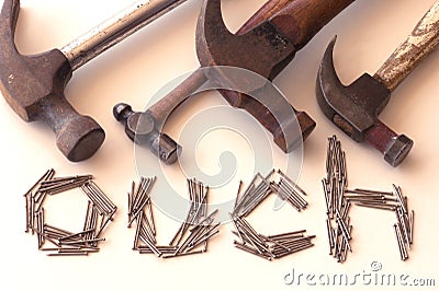 Word `ouch` with four old hammers and small nails acts as a warning to be careful. Stock Photo