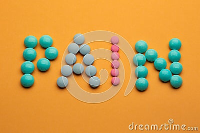 Word pain on orange background written with colorful pills. Painkiller tablets taken by prescription Stock Photo