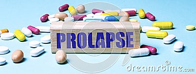 The word PROLAPSE is written on a wooden block on a light blue background among multi-colored pills. Medical concept Stock Photo