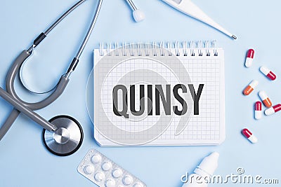 The word quinsy written on a white notepad on a blue background near a stethoscope, syringe, electronic thermometer and pills. Stock Photo