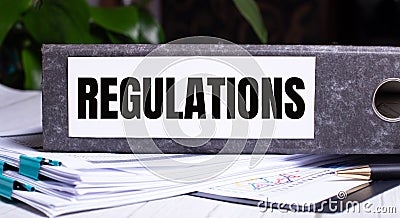 The word REGULATIONS is written on a gray file folder next to documents. Business concept Stock Photo