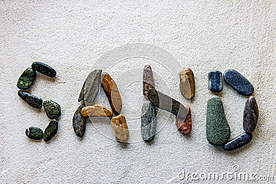 Word SAND is written using colored stones on a white sandy surface Stock Photo