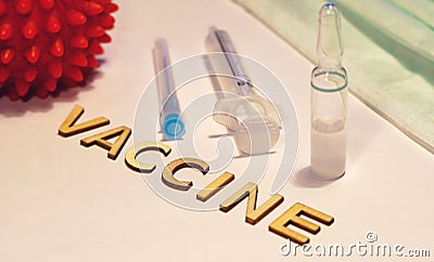 The word vaccine is laid out on a hundred table surrounded by an ampoule and syringe Stock Photo