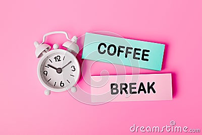 The words Coffee Break written on paper note near white alarm clock on pink background. Closeup of a personal agenda Stock Photo