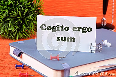 The words Cogito Ergo Sum or I think Therefore I Am on a white business card standing on a notepad Stock Photo
