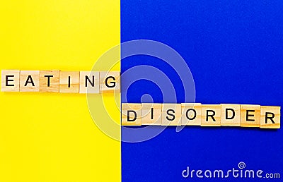 Words eating disorder. Wooden blocks with an inscription on top on a yellow and blue background. Social problems of teenagers Stock Photo