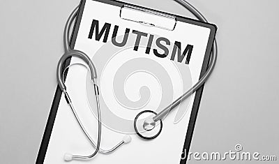 The words mutism is written on white paper on a grey background near a stethoscope. Medical concept Stock Photo