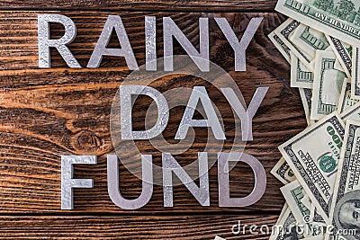 Words RAINY DAY FUND laid on wooden surface by metal letters with rain drops and us dollar banknotes Stock Photo
