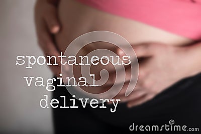 Words SPONTANEOUS VAGINAL DELIVERY. Young pregnant between 30 and 35 years old woman touches her belly in the background Stock Photo