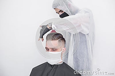 The work of the barber during the coronavirus, the hairdresser trim the client in a mask and a protective suit, quarantine Stock Photo