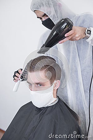 The work of the barber during the coronavirus, the hairdresser trim the client in a mask and a protective suit, quarantine Stock Photo