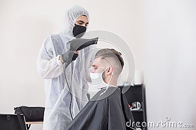 The work of the barber during the coronavirus, the hairdresser trim the client in a mask and a protective suit, quarantine Stock Photo