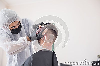 The work of the barber during the coronavirus, the hairdresser trim the client in a mask and a protective suit, quarantine Stock Photo