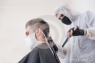 The work of the barber during the coronavirus, the hairdresser trim the client in a mask and a protective suit, quarantine Stock Photo