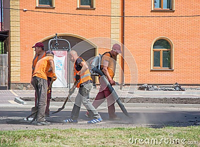 Work brigade using tools for spreading asphalt crumb into the holes in the road. A worker blowing out dust from the holes in the r Editorial Stock Photo