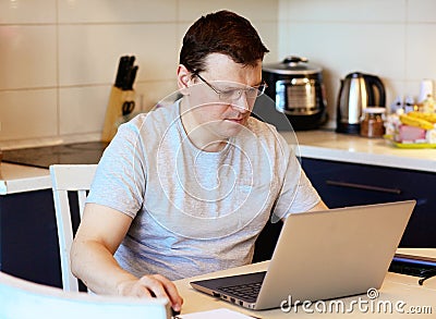 Work at home online during a pandemic 2019-ncov. Focused and serious young man in glasses working on laptop while sitting Stock Photo