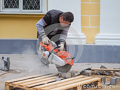 Work on laying the new tile on a city street. Lays the new tile on the floor. Paving in the city. Worker sawing the tiles. Russia. Editorial Stock Photo