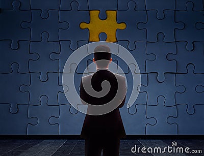 Work Problem Concept. Blurred Back side of a businessman Standing in front of blank Jigsaw Puzzle Wall to Finding a Lost Piece. T Stock Photo