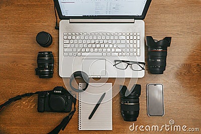 Work space photographer with laptop, digital camera, lenses, notebook, glasses, pen, phone and camera accessory. view on dark wood Editorial Stock Photo