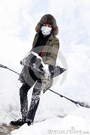 Winter Concepts. Workaholic Caucasian Handsome Man in Protective Facial Mask Throwing Away Snow With Broken Shovel In City Stock Photo