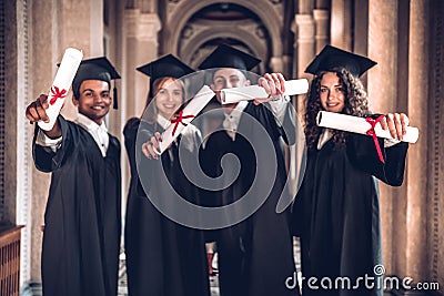 We worked hard and got results!Group of smiling graduates showing their diplomas ,standing together in university hall and looking Stock Photo